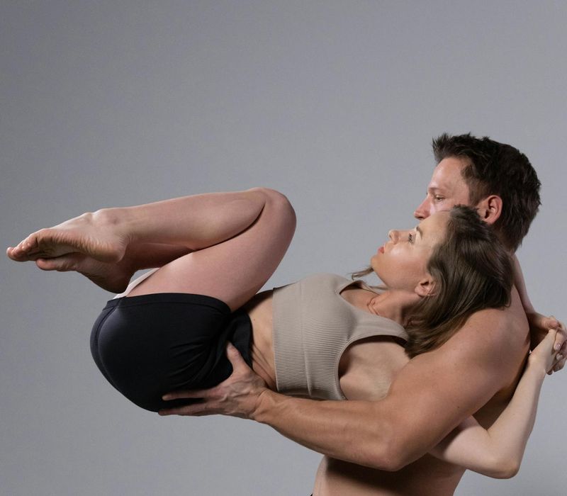 Silhouette of a couple holding a challenging partner yoga pose against a sunset.